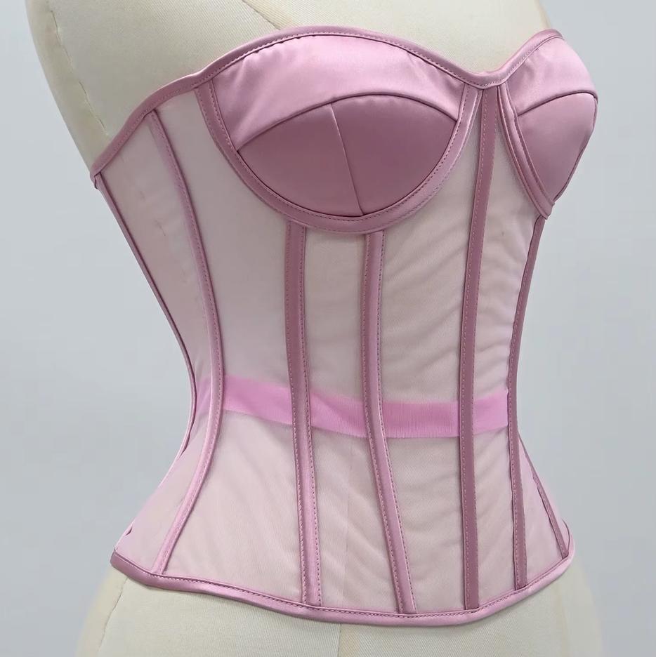 The Lilah light pink corset with satin-like panels and sheer mesh sections, displayed on a cream-colored dress form against a light gray background.
