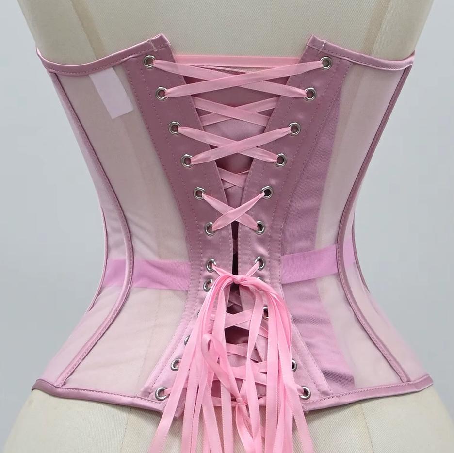 The Lilah pink corset-style harness with sheer mesh panels, structured fabric, and pink ribbon laces with metal eyelets, shown on a mannequin torso against a light gray background.