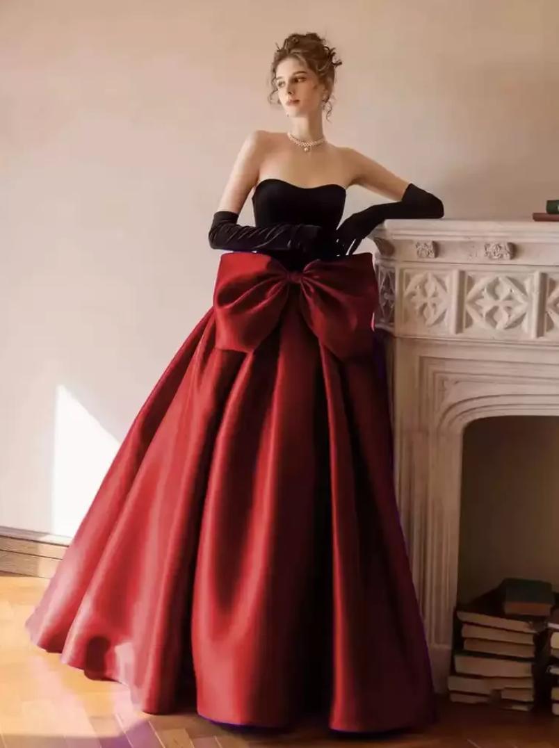 Strapless two-tone satin A-line gown featuring a black bodice, red floor-length skirt, and an oversized bow at the waist.
