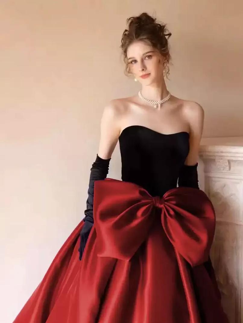 Strapless two-tone satin gown with a black bodice, red A-line skirt, and an oversized red bow at the waist.