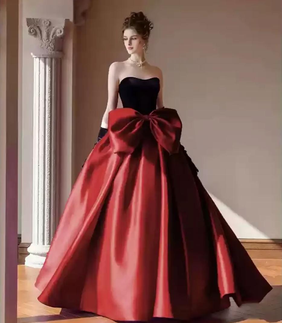Strapless two-tone satin A-line gown with a black bodice, red floor-length skirt, and an oversized red bow at the waist.