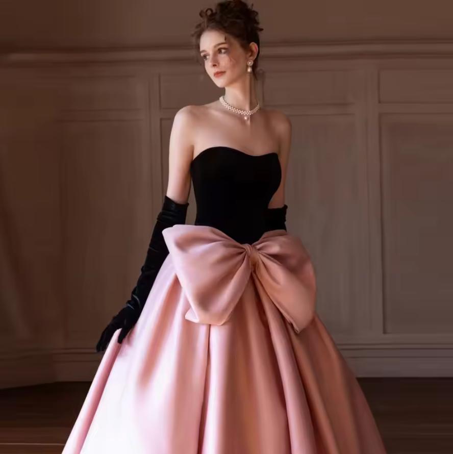 Strapless two-tone satin gown with a black bodice, pink A-line skirt, and an oversized bow at the waist.