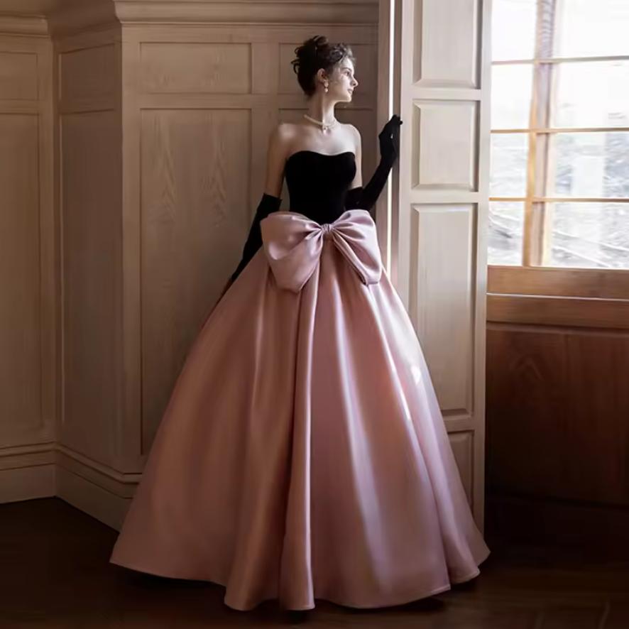 Strapless two-tone satin gown with a black bodice, pink A-line skirt, and an oversized bow at the waist.