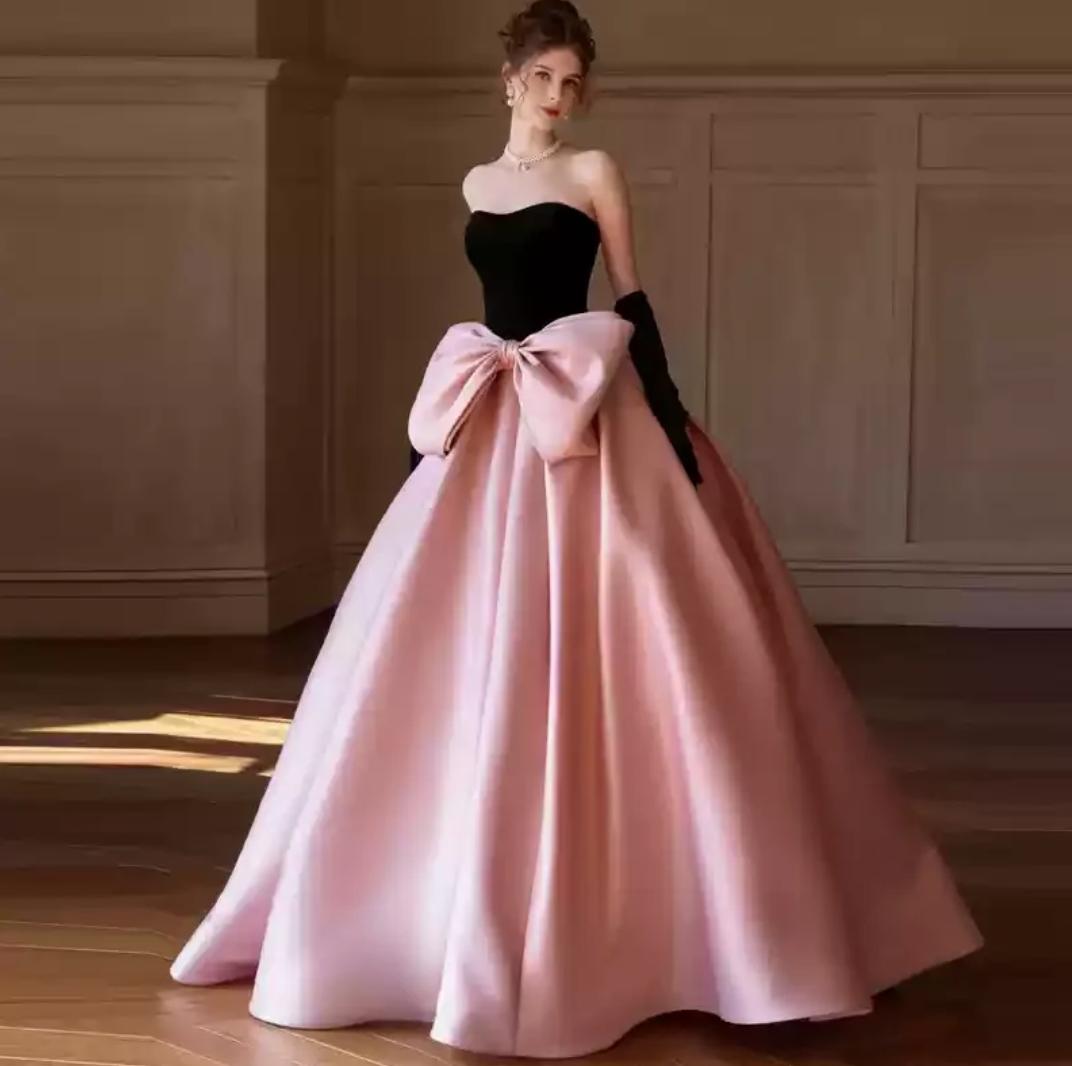 Strapless two-tone A-line gown with a black bodice, pink satin floor-length skirt, and an oversized bow at the waist.