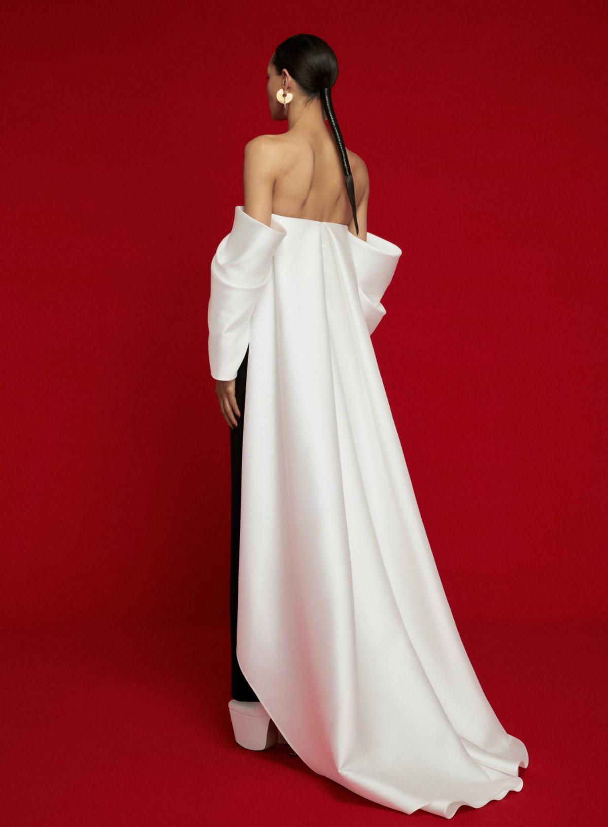 Model wearing a strapless white satin evening gown with a dramatic court train against a red background.