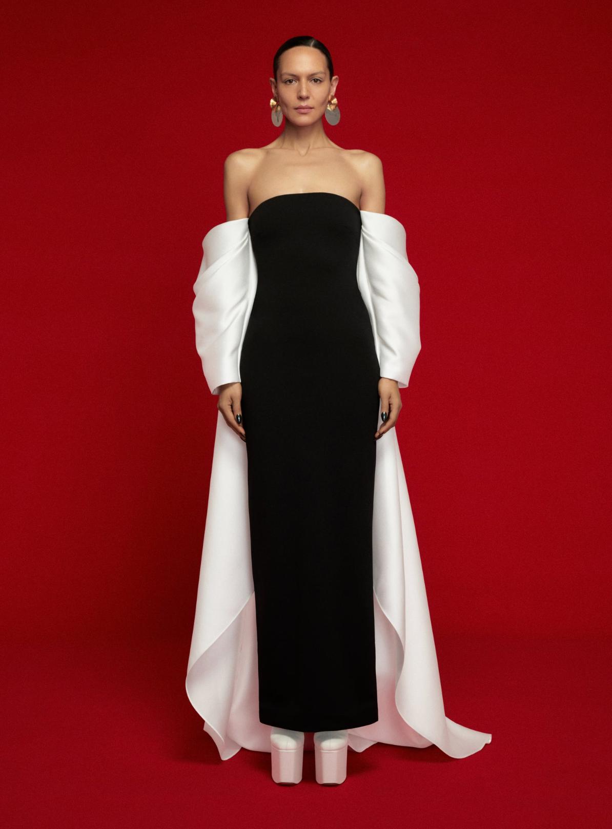 Model wearing a strapless black satin evening gown with dramatic white off-the-shoulder sleeves and a court train.