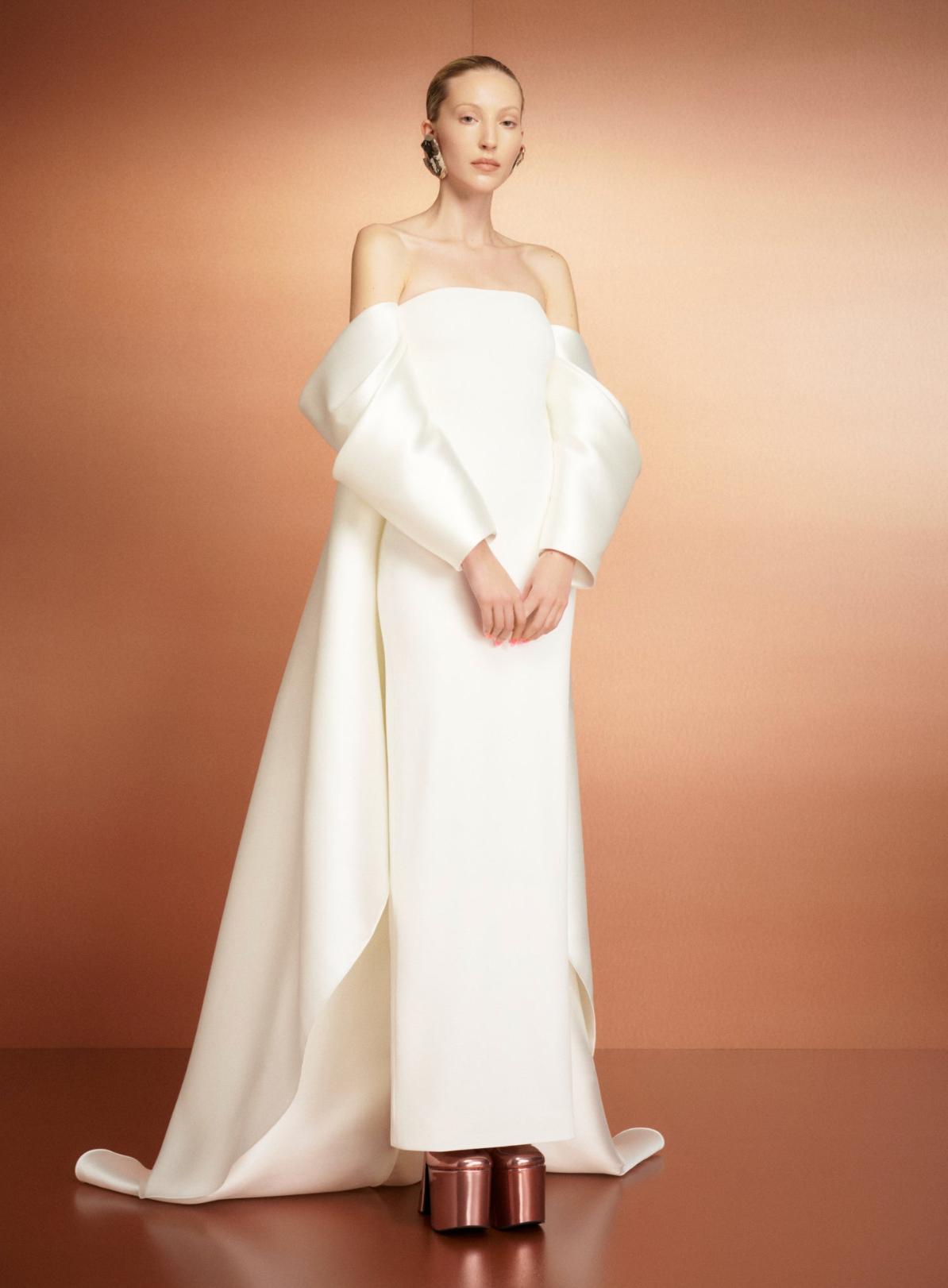 Model wearing a strapless white satin evening gown with dramatic off-the-shoulder sleeves and a flowing court train.