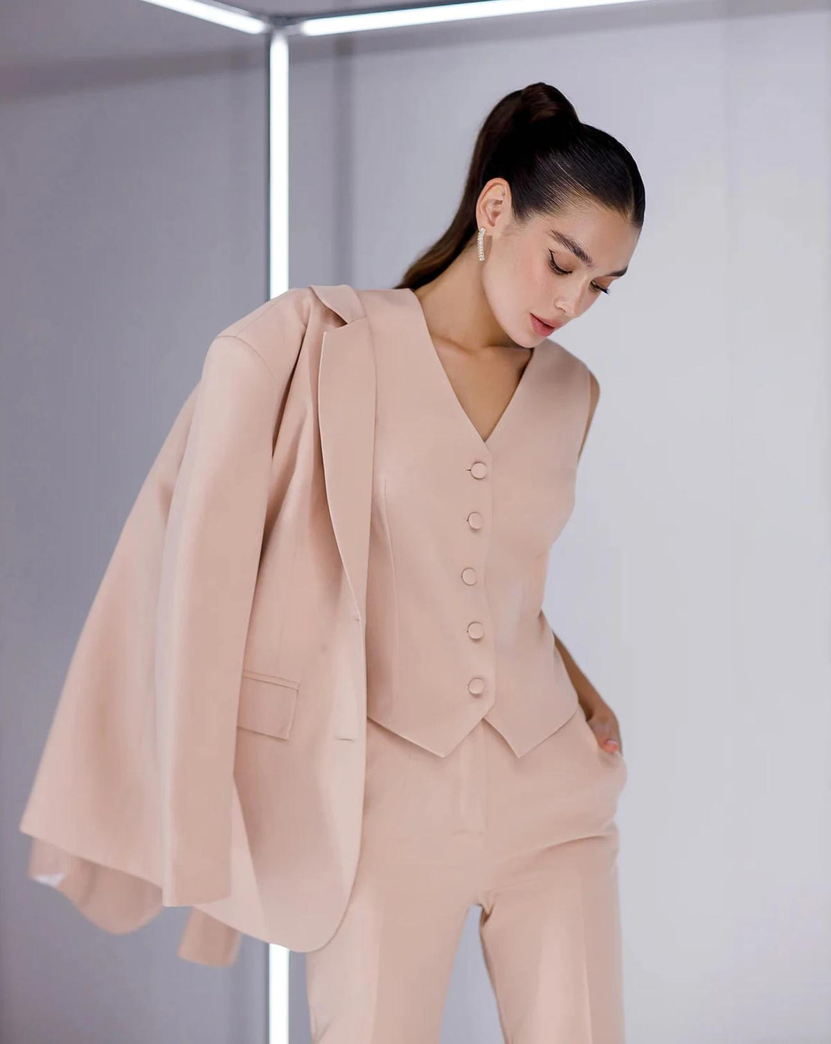 Model wearing a blush pink three-piece serge suit featuring a tailored vest, matching trousers, and a draped blazer.