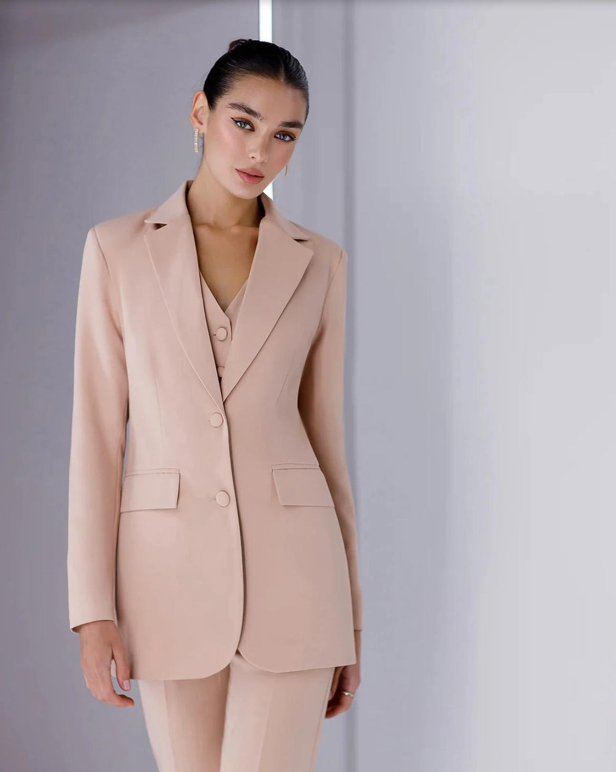Model wearing a beige three-piece serge suit featuring a single-breasted blazer, matching vest, and tailored trousers.