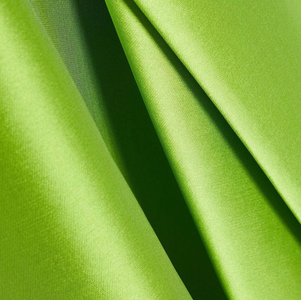 Close-up of vibrant lime green Mikado satin twill fabric with elegant, flowing folds and a smooth, polished texture.