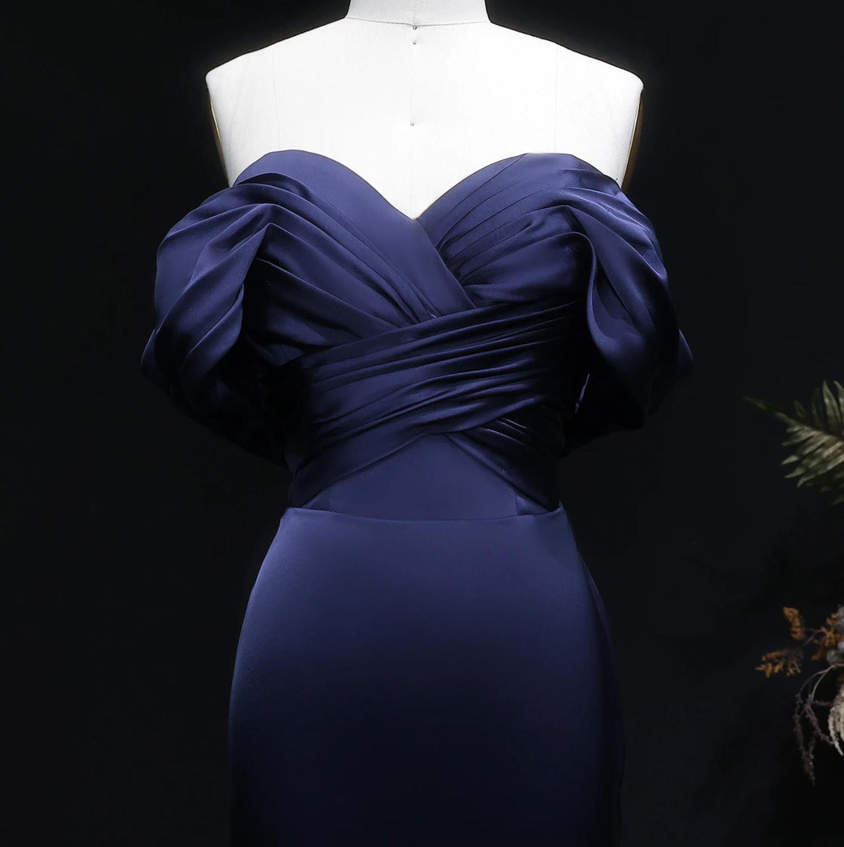 Navy blue satin mermaid evening gown with an off-shoulder pleated bodice on a mannequin.