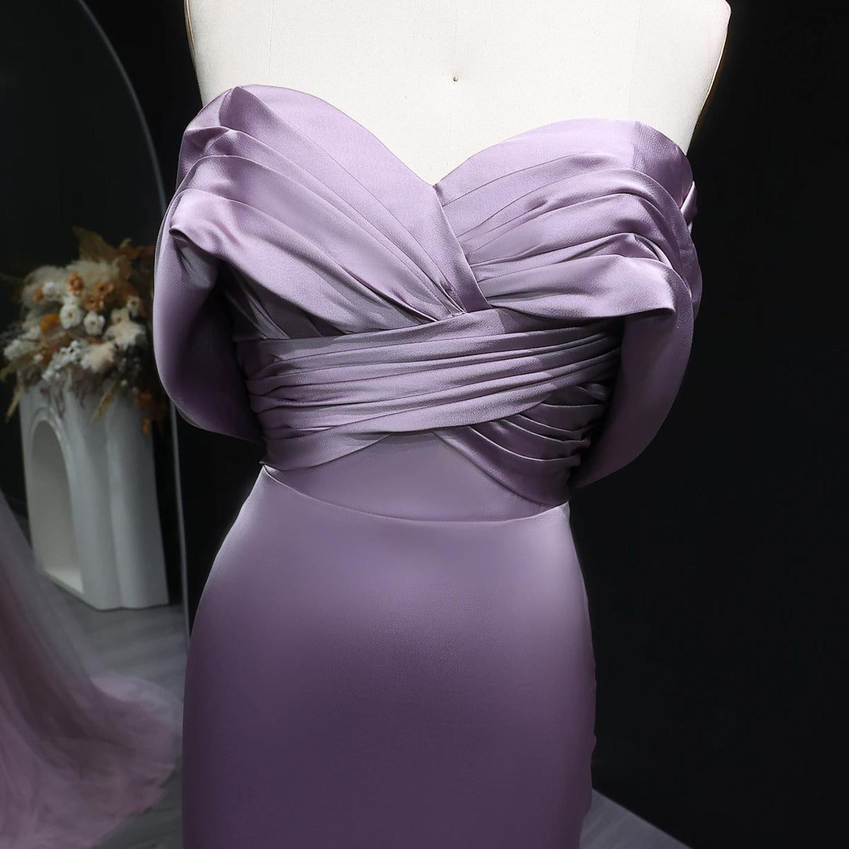 Lavender satin mermaid evening gown with an elegant off-shoulder neckline and delicate bodice pleating on a mannequin.