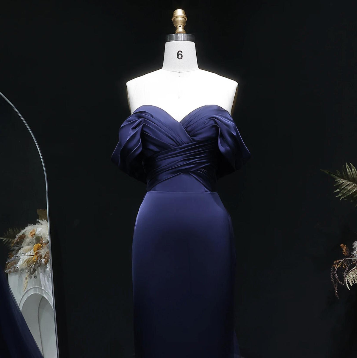 Elegant navy blue satin mermaid evening gown with an off-shoulder pleated bodice on a mannequin.