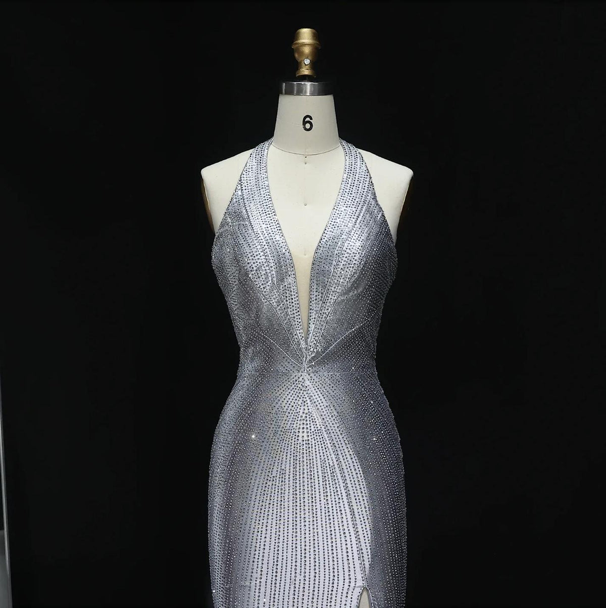 Silver satin halter evening gown featuring a deep V-neckline and intricate sparkling crystal appliqué detailing.