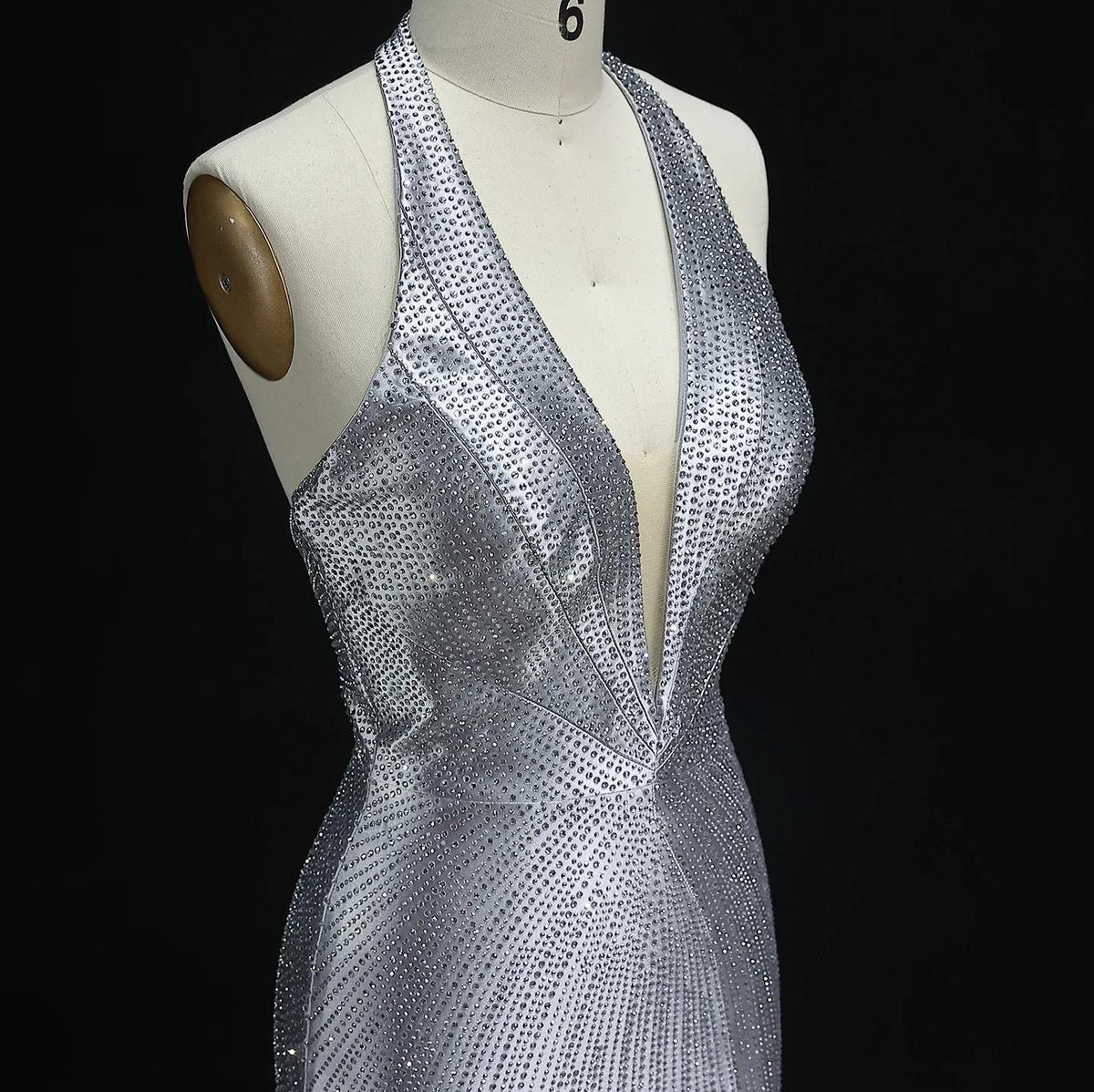 Silver satin halter evening gown featuring a deep V-neckline and intricate crystal embellishments on a dress form.