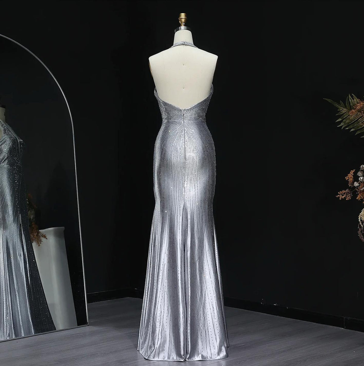 Backless silver satin evening gown with a halter neckline and vertical crystal embellishments on a mannequin.