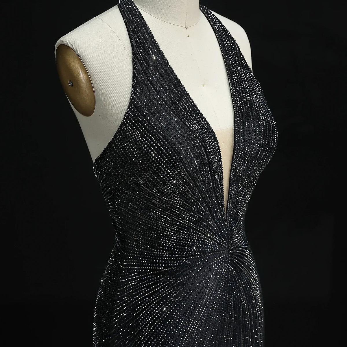 Black satin halter evening gown with a deep V-neck and sparkling crystal embellishments on a dress form.