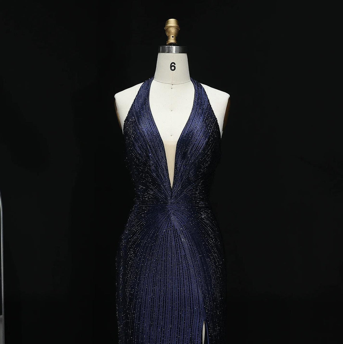Midnight blue satin evening gown with crystal embellishments, halter neckline, and deep-cut bodice on a mannequin.
