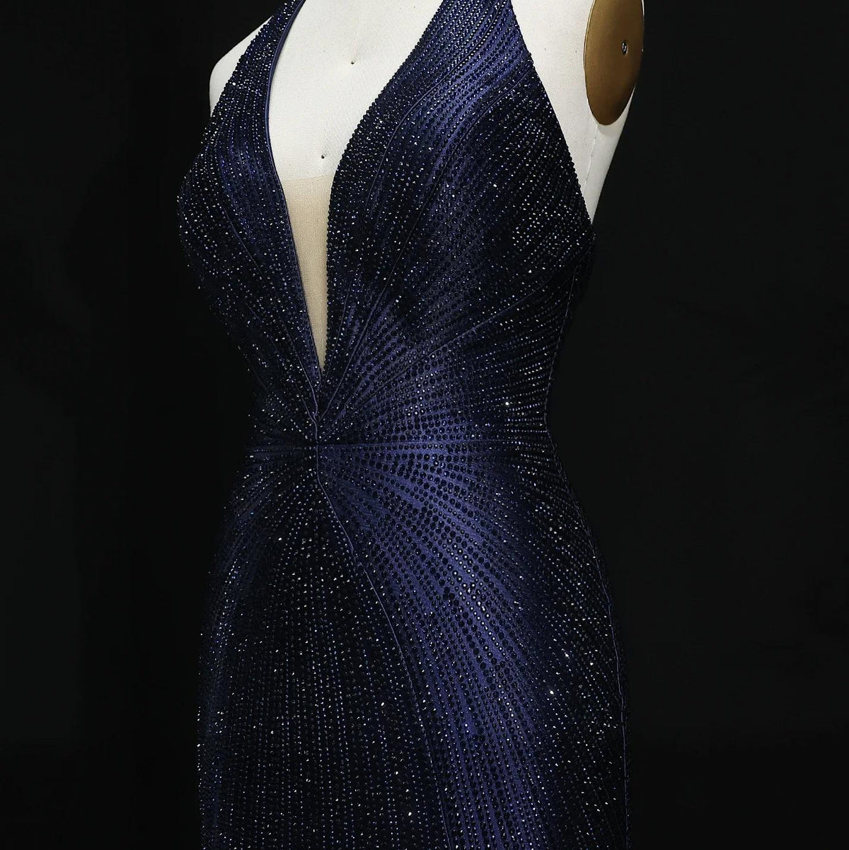Midnight blue satin evening gown with a plunging halter neckline and intricate crystal embellishments on a mannequin.