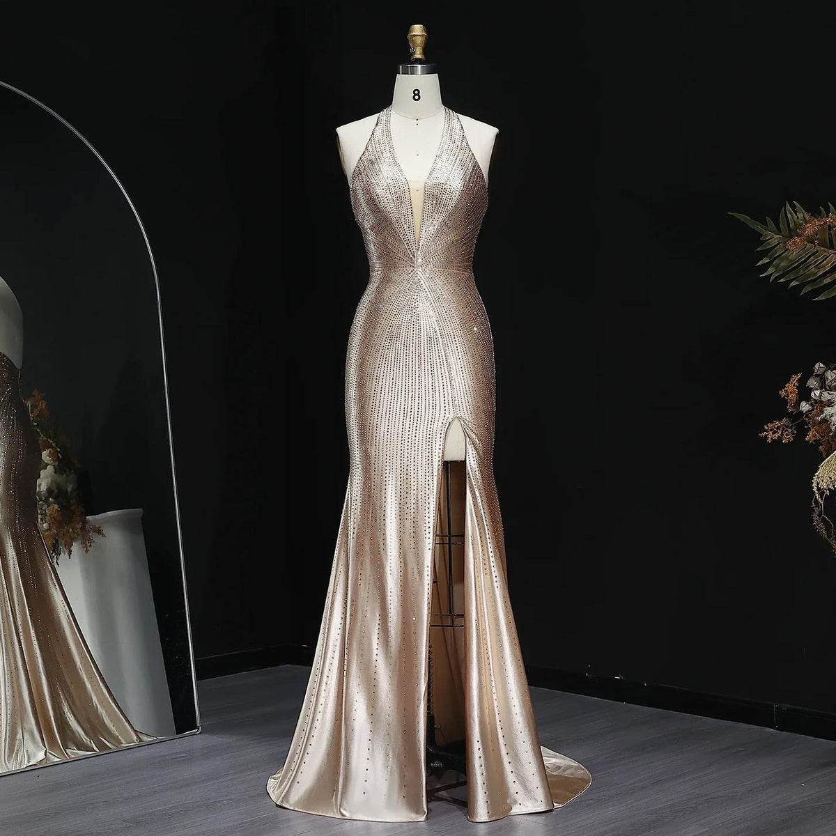 Champagne satin evening gown with crystal embellishments, halter neckline, and a high thigh slit on a dress form.