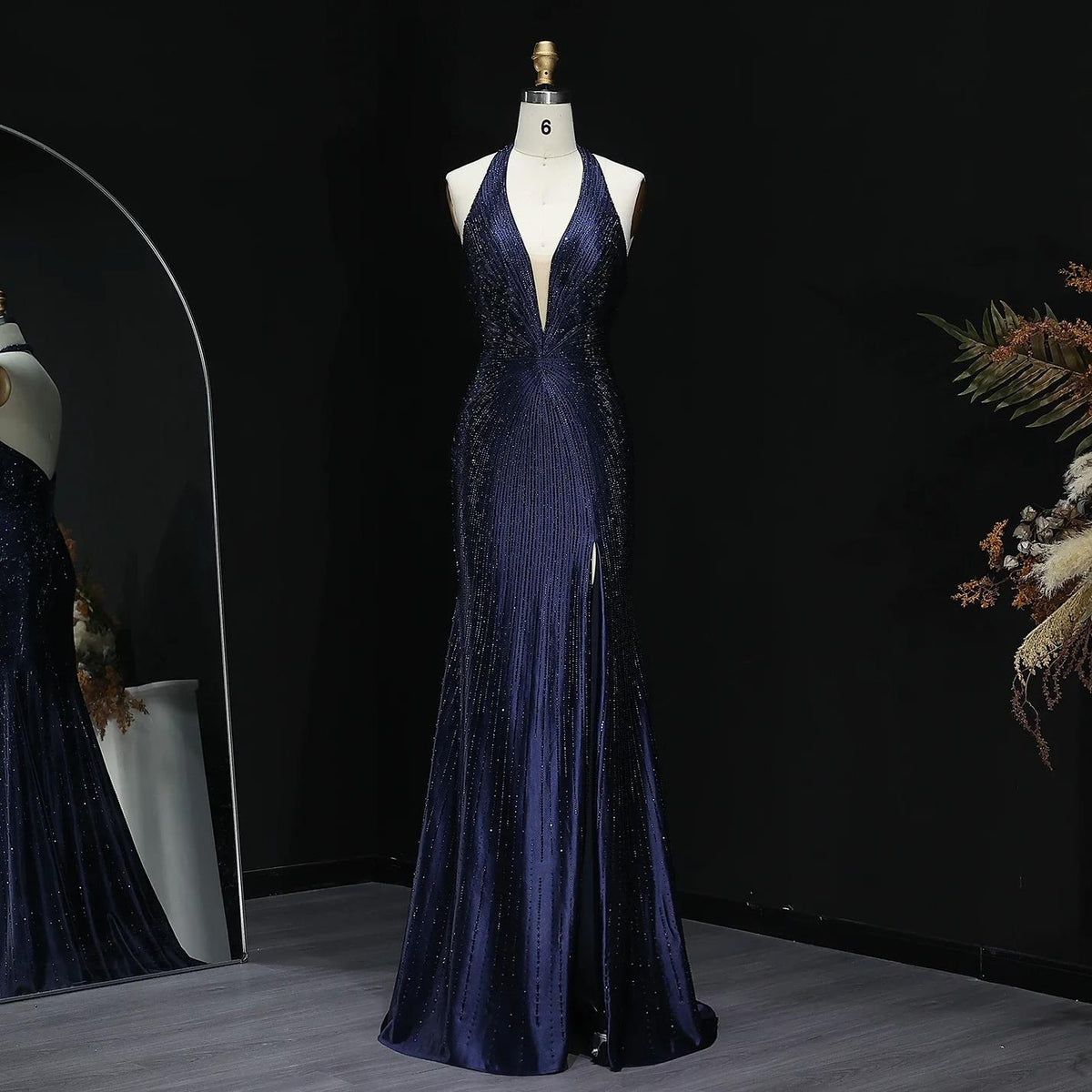 Midnight blue satin evening gown with a plunging halter neckline, crystal embellishments, and a thigh-high slit on a mannequin.