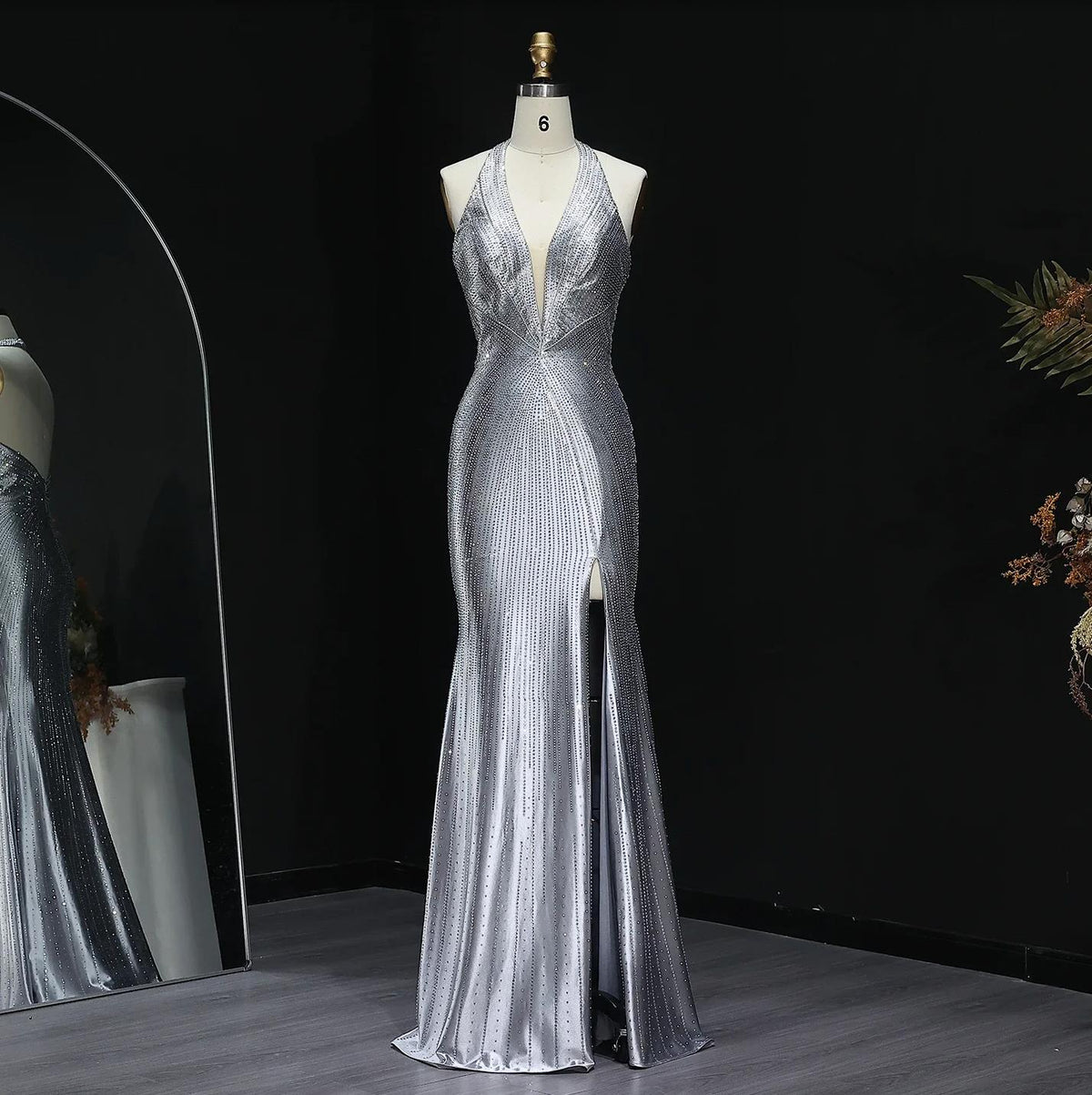 Silver satin evening gown with crystal embellishments, halter neckline, deep V-neck, and a high thigh slit on a mannequin.