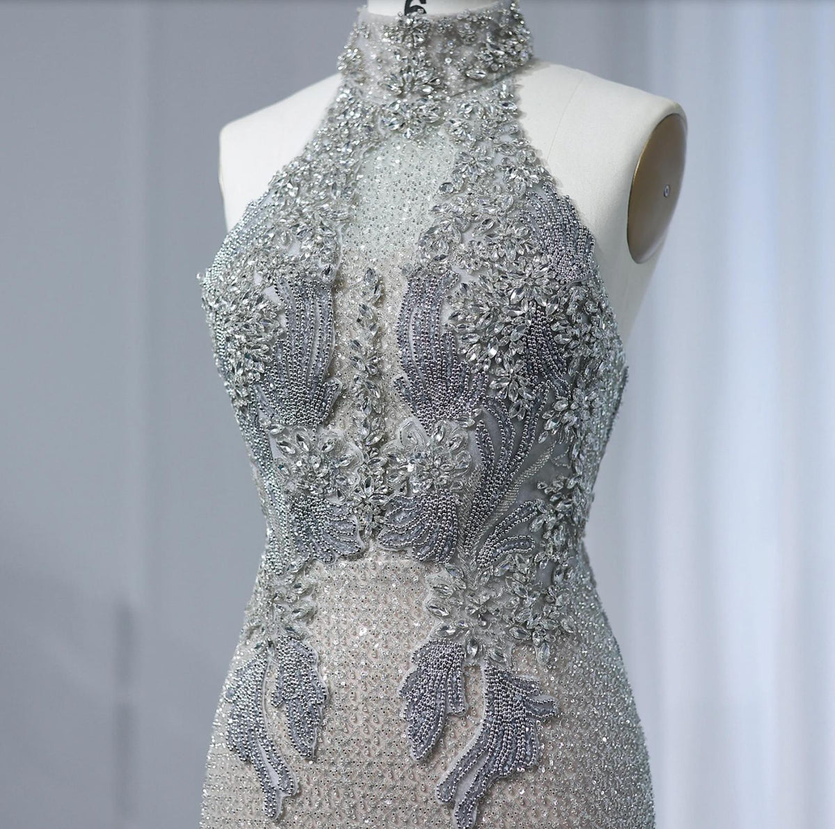 Silver halter-neck gown featuring intricate crystal, pearl, and bead embellishments on sheer tulle fabric.