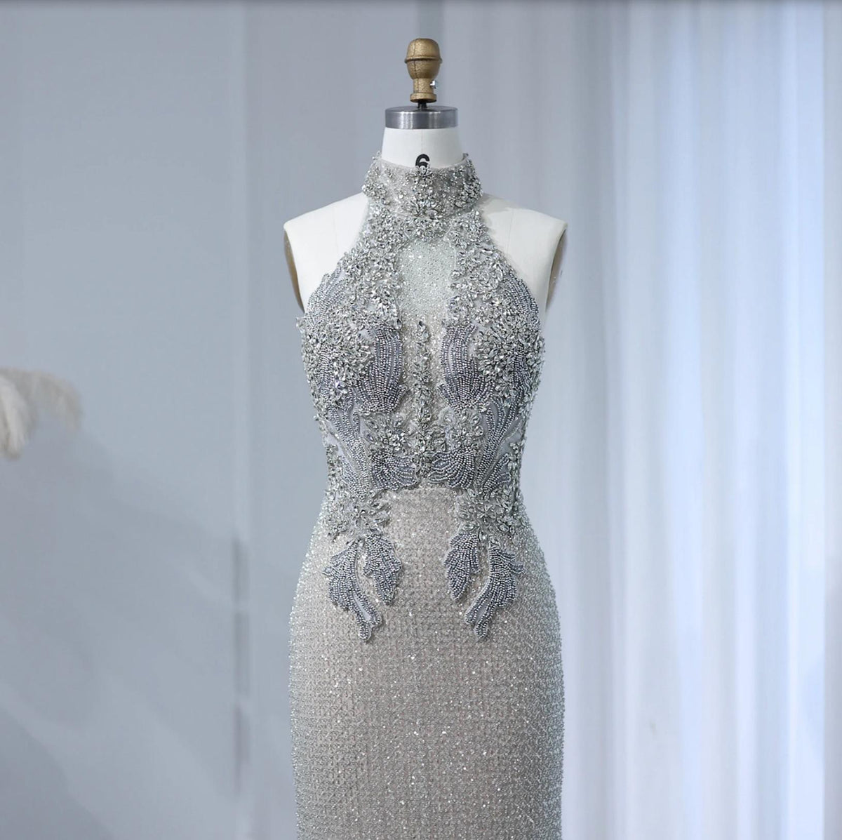 Silver sleeveless A-line gown with intricate crystal beading, pearls, and a high halter neckline on a mannequin.