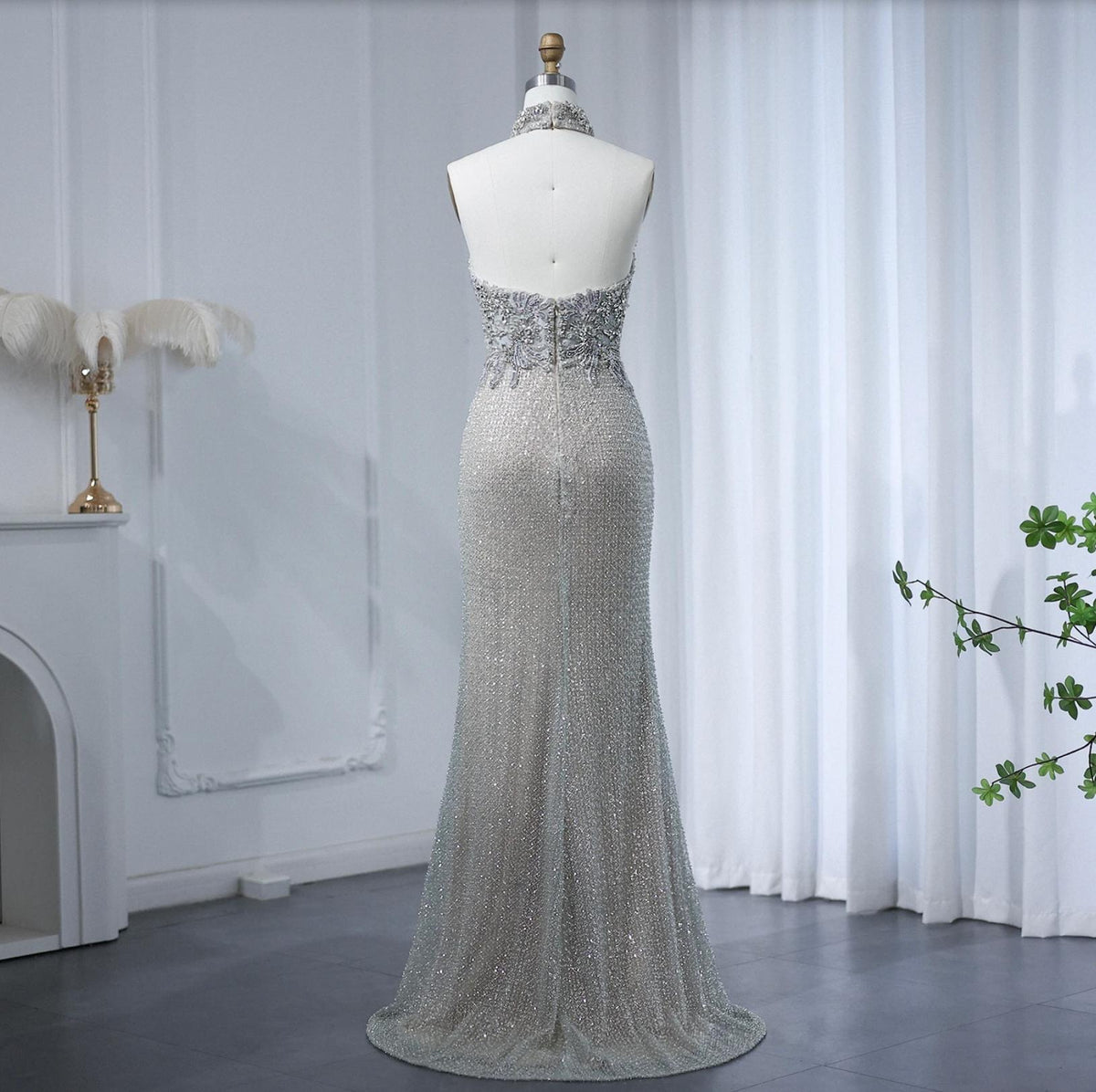 Backless silver floor-length gown with intricate beadwork, crystals, and a halter neckline on a mannequin.