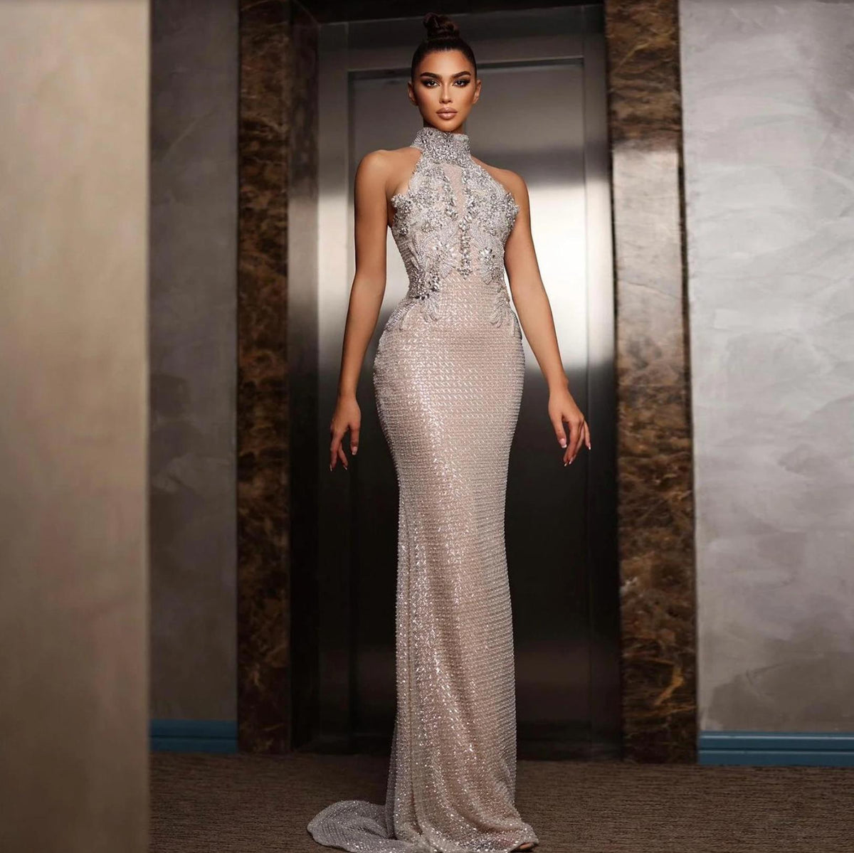 Floor-length silver A-line gown with a halter neckline, intricate crystal beading, and shimmering tulle fabric.