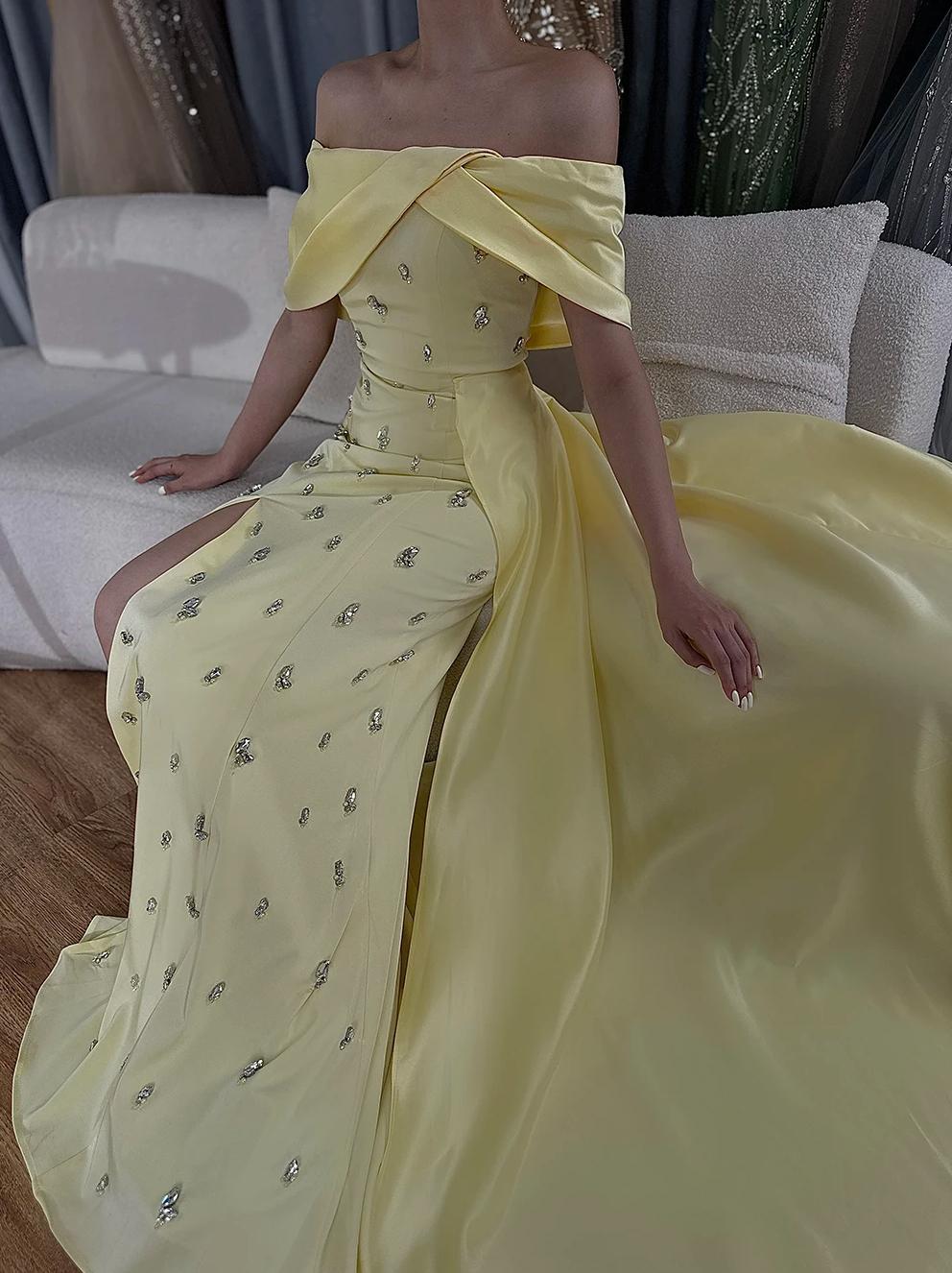 Off-shoulder yellow satin gown with a crystal-beaded overskirt and a high-slit A-line silhouette.