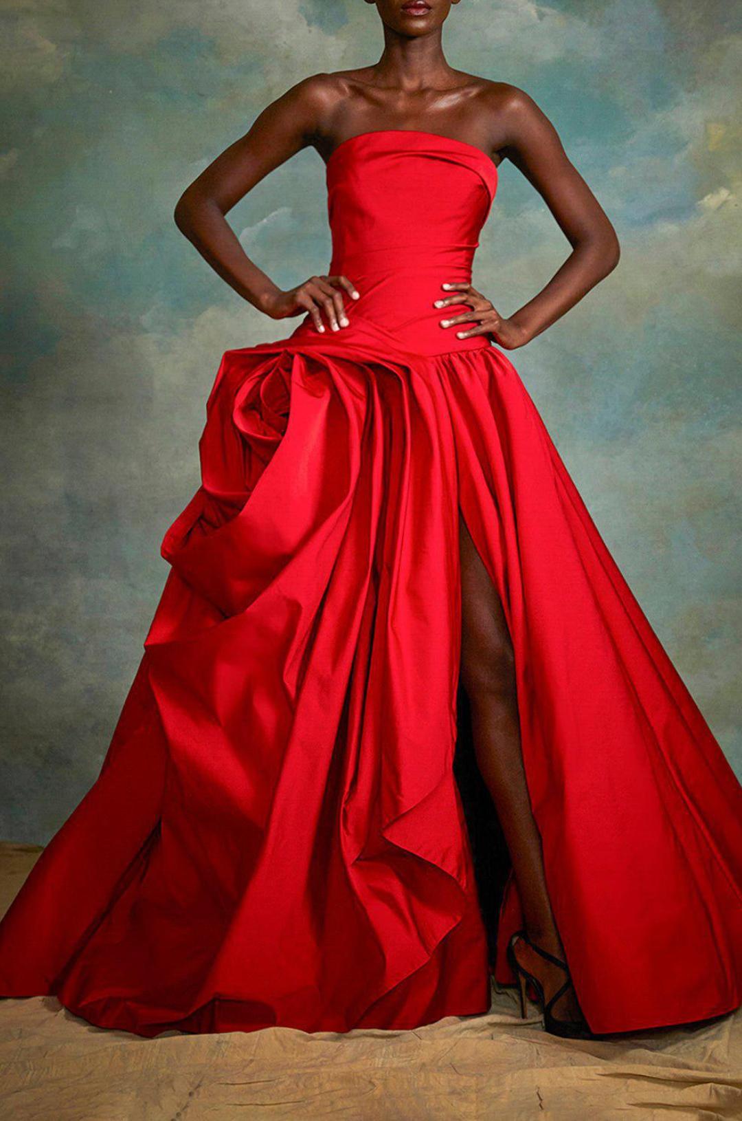 Red strapless gown with hand-draped rose detail, side slit, and luxurious fabric for a formal silhouette.