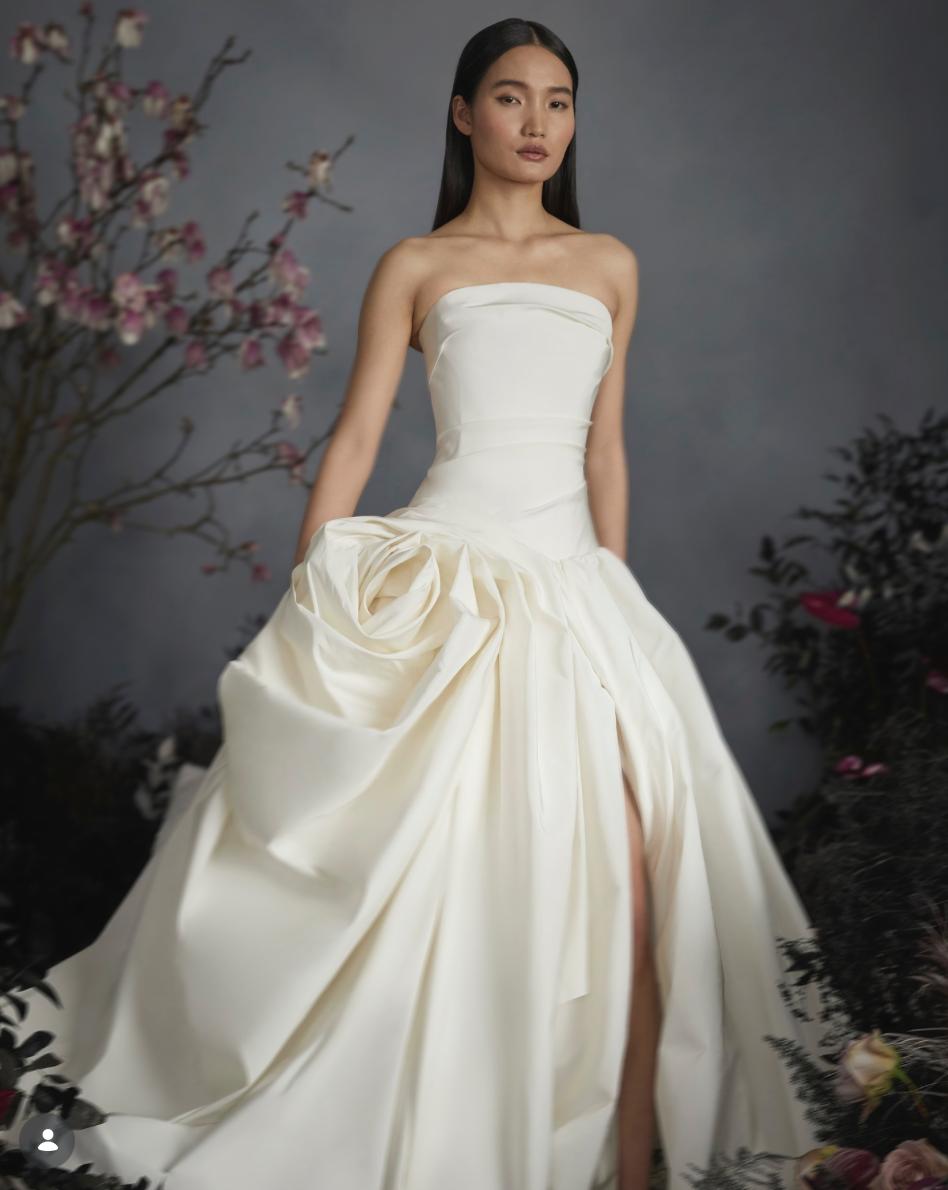 Strapless ivory crepe gown featuring a hand-draped rose detail at the hip and a sophisticated side slit.