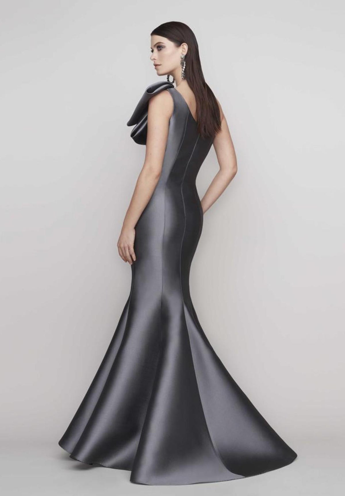 Charcoal grey one-shoulder satin gown with a dramatic shoulder bow and a sculpted, fluted floor-length skirt.