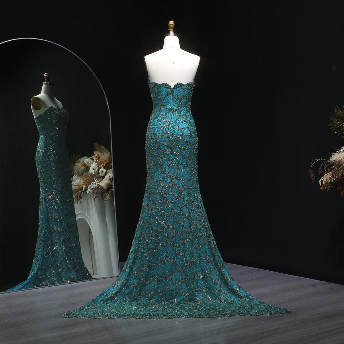 Emerald green strapless mermaid gown with intricate crystal beading, tulle fabric, and a sweeping train on a mannequin.