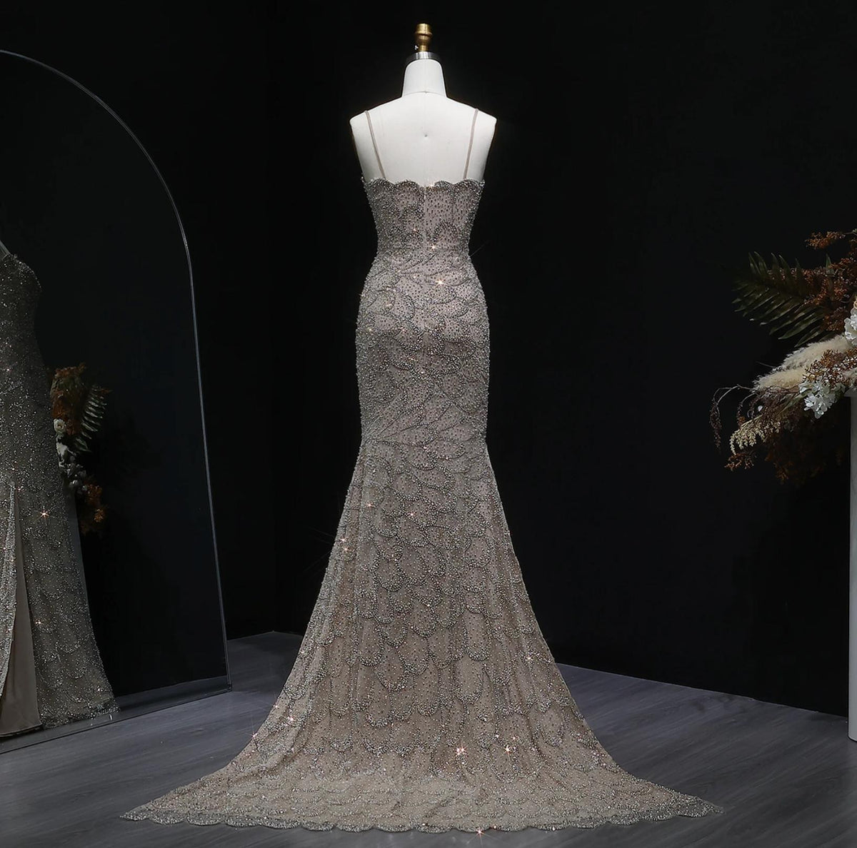 Emerald green strapless mermaid gown with intricate crystal beading, tulle, and a sweeping train on a mannequin.