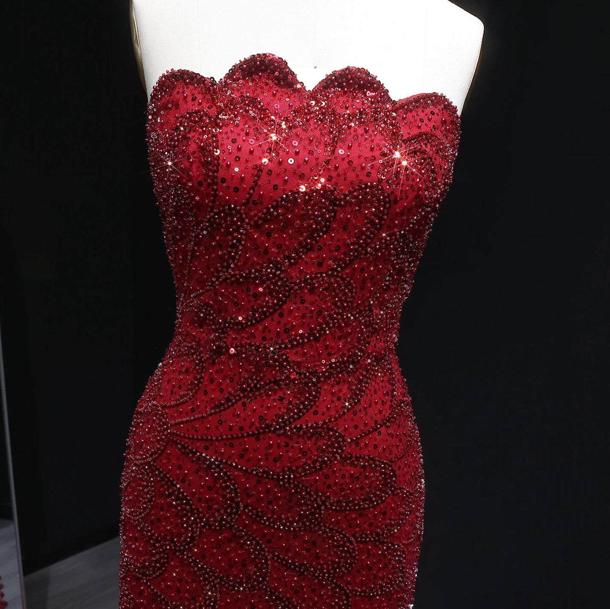 Strapless red mermaid gown featuring intricate crystal beadwork and sequin appliqués on a fitted tulle and satin bodice.