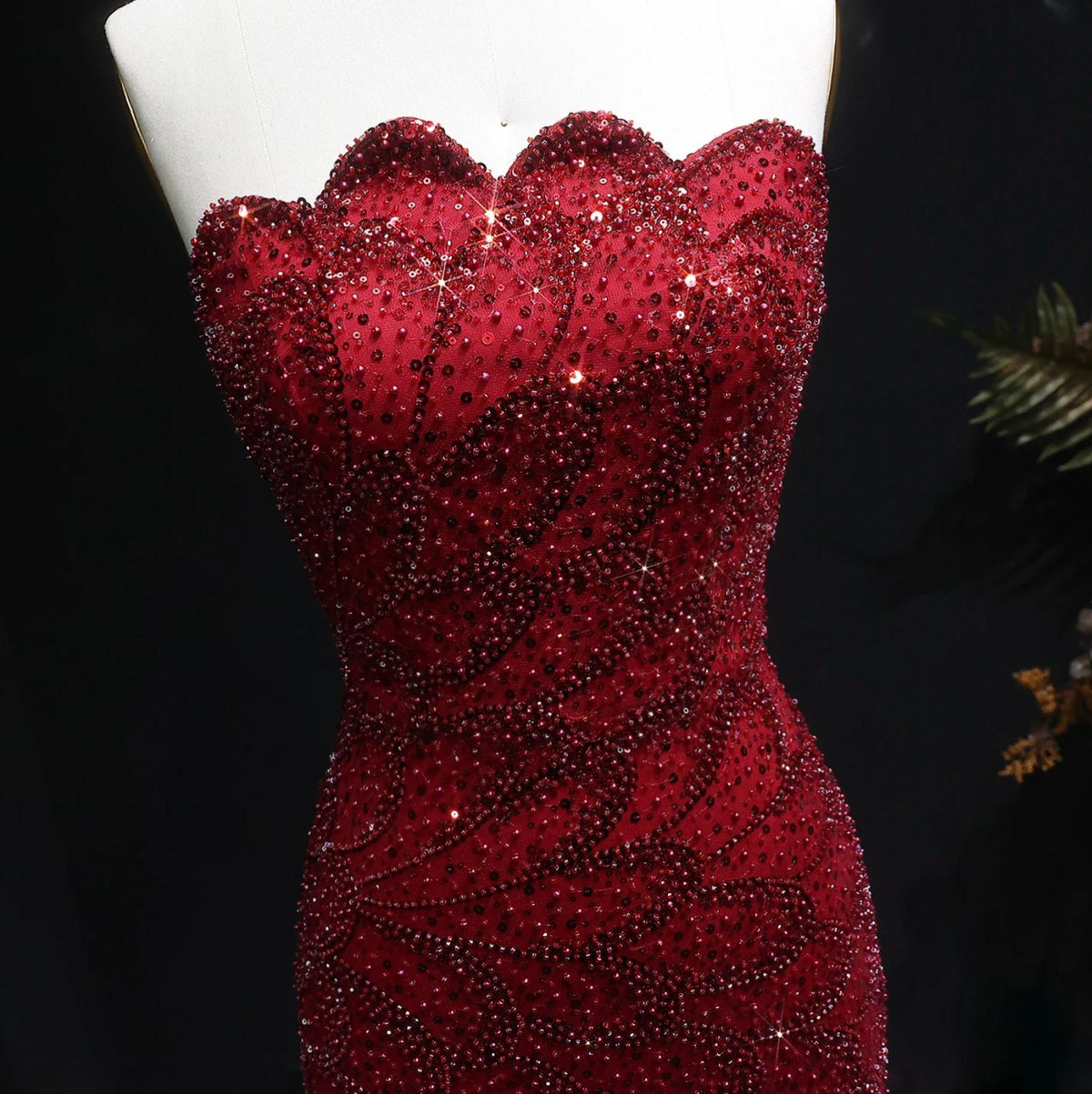 Strapless deep red mermaid gown featuring intricate crystal beading and sequin appliqués on tulle and satin fabric.