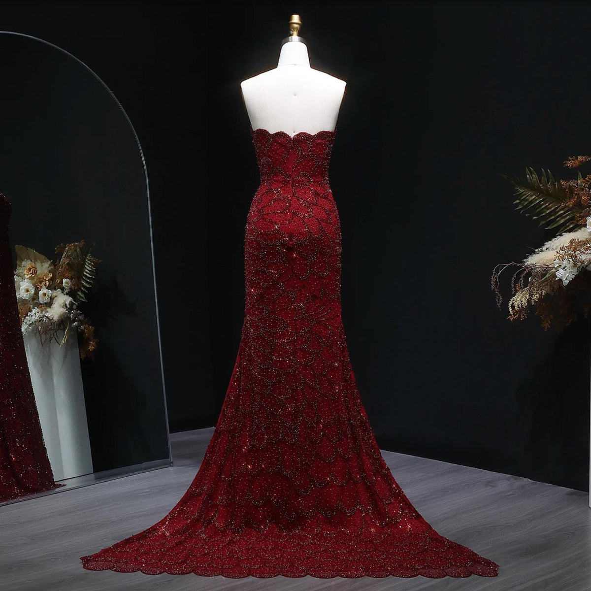 Strapless deep red mermaid gown with intricate crystal beading, tulle fabric, and a sweeping train on a mannequin.