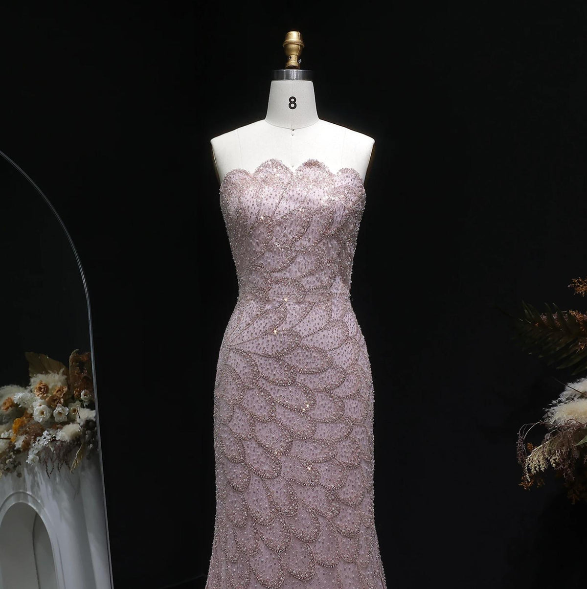 Strapless blush pink mermaid gown featuring intricate crystal beading and scalloped patterns on a mannequin.