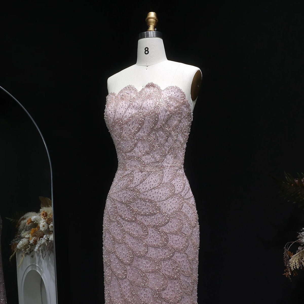 Strapless blush pink mermaid gown featuring intricate crystal beadwork and scalloped patterns on a mannequin.