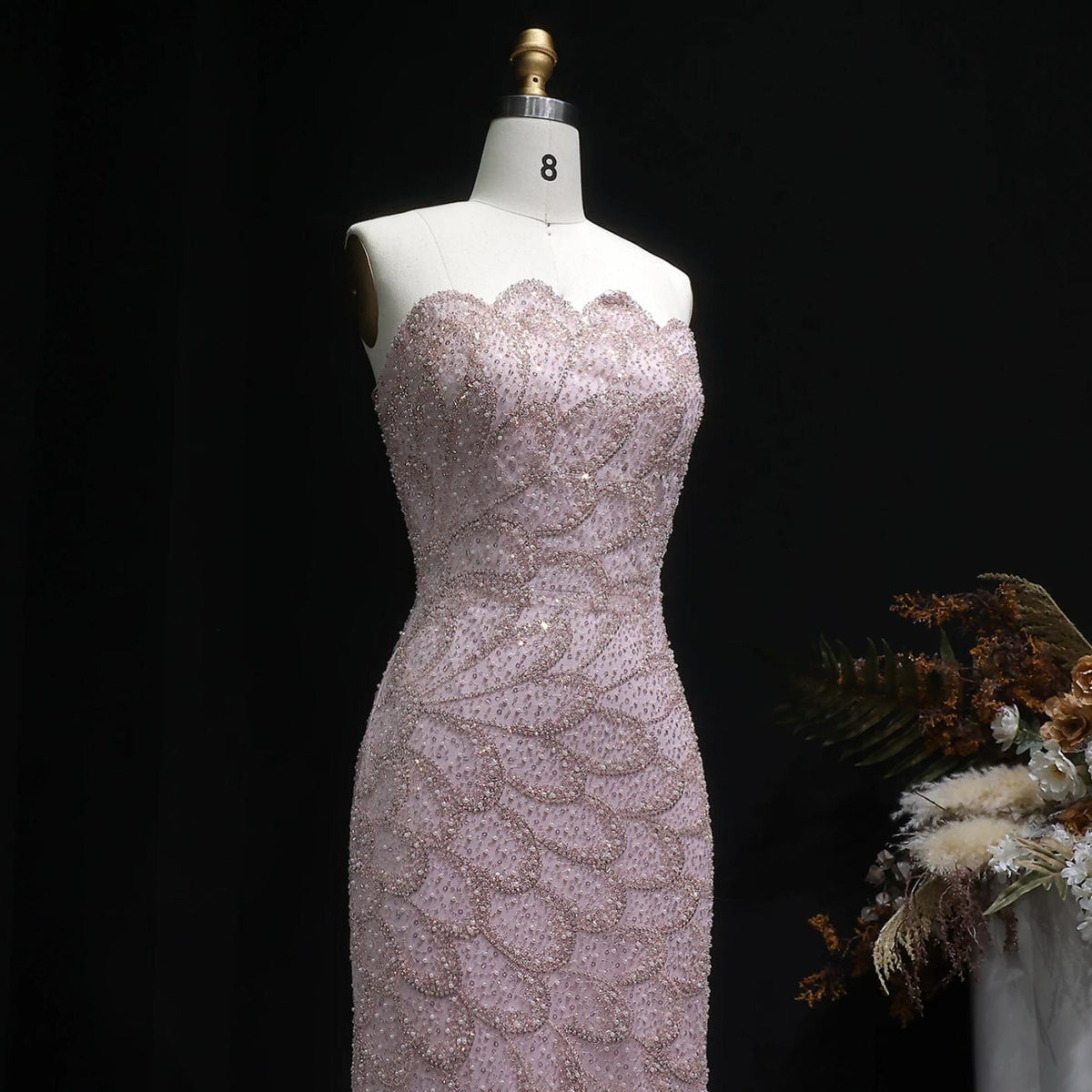 Strapless blush pink mermaid gown featuring intricate crystal beadwork and scalloped patterns on a mannequin.