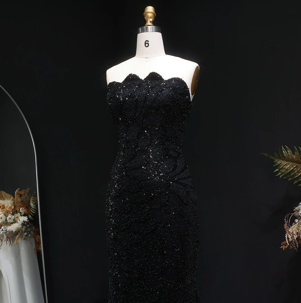Strapless black mermaid gown featuring intricate crystal beadwork and lace appliqués on a mannequin.