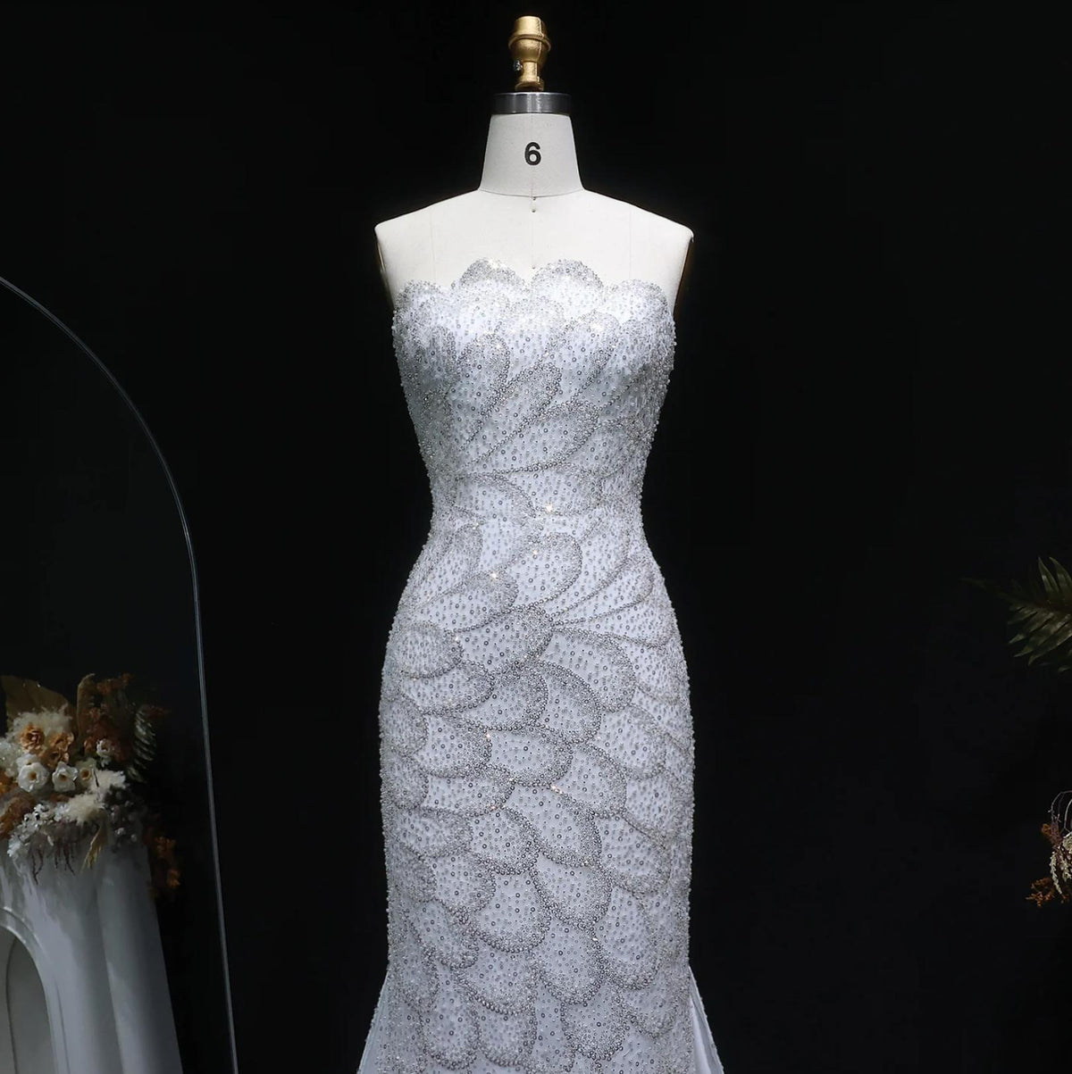 Strapless emerald green mermaid gown with intricate crystal beading and tulle detailing on a mannequin.
