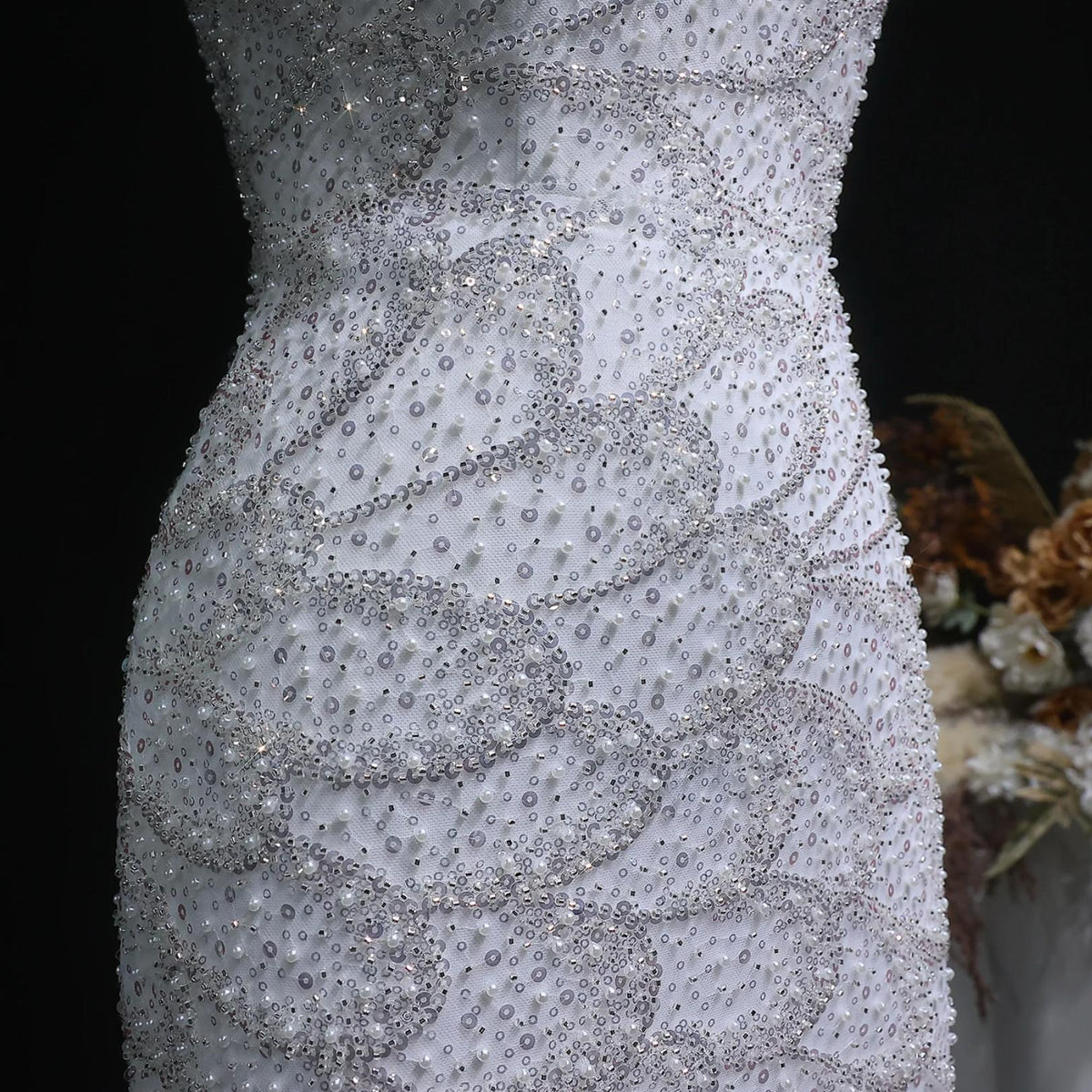 Close-up of a white mermaid gown featuring intricate silver sequin patterns, pearl beads, and crystal appliqués.
