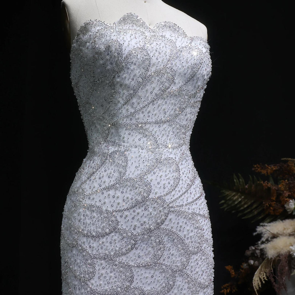 Strapless white mermaid gown featuring intricate crystal beading and sequin appliqués on a tulle and satin bodice.