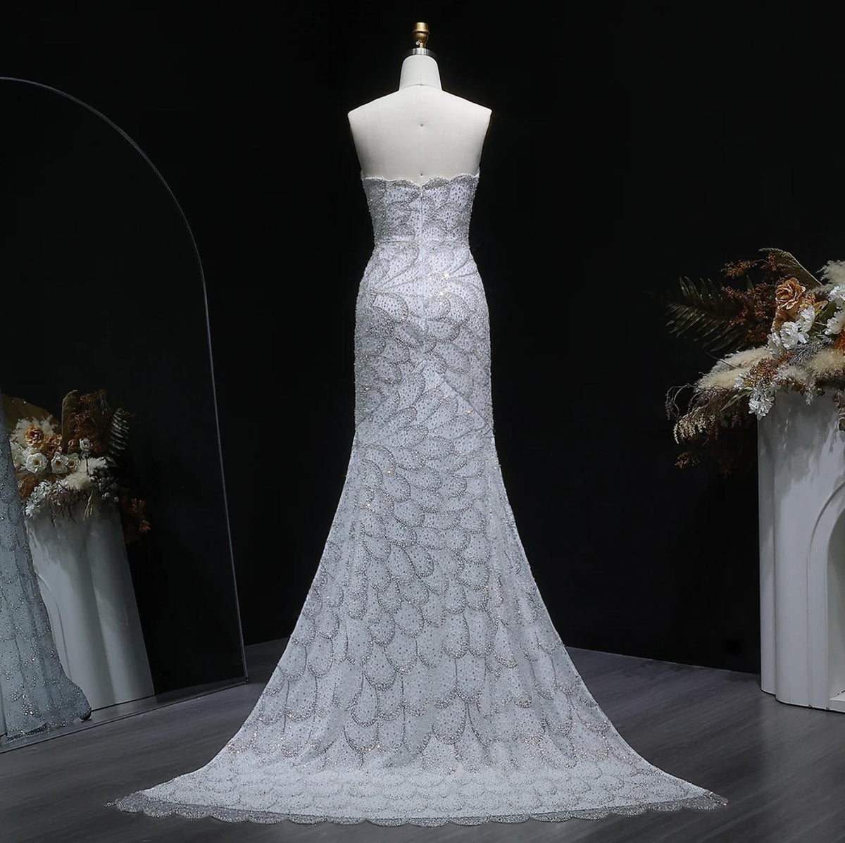 Strapless emerald green mermaid gown with intricate crystal beading, tulle fabric, and a sweeping train on a mannequin.
