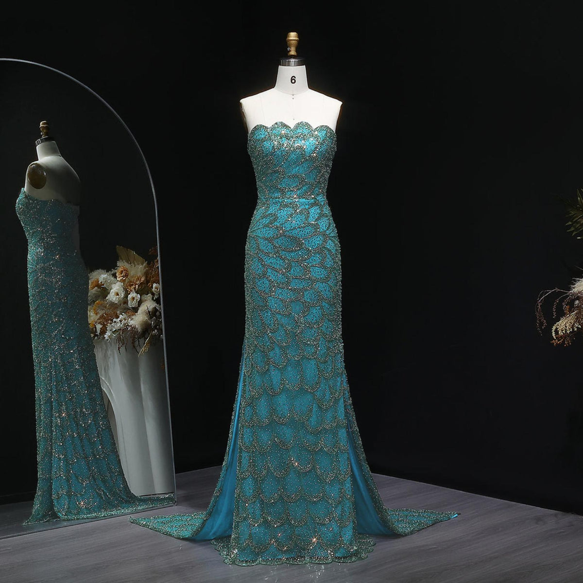 Emerald green strapless mermaid gown with intricate crystal beading, tulle fabric, and a sweeping train on a mannequin.