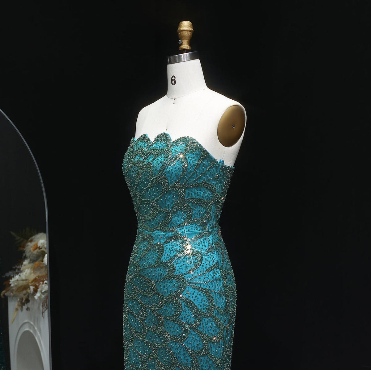 Emerald green strapless mermaid gown with intricate crystal beading and tulle detailing on a mannequin.