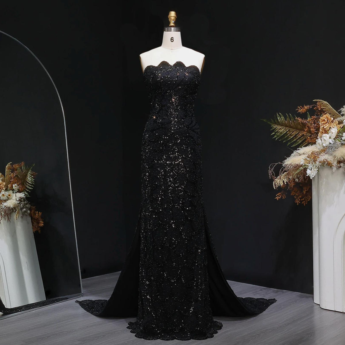 Strapless black mermaid gown featuring intricate crystal beading, tulle fabric, and a sweeping train on a mannequin.